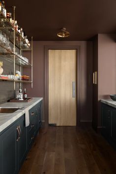 an empty kitchen with wooden floors and purple walls, along with shelves filled with bottles