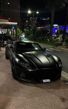 the black sports car is parked on the side of the road at night in front of some buildings