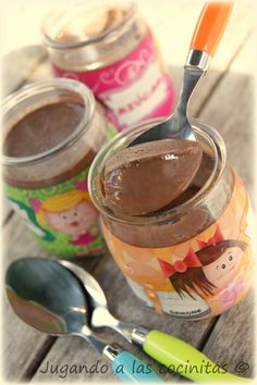 two jars filled with chocolate pudding and spoons next to each other on a wooden table