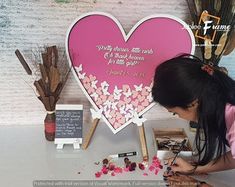 a woman is painting flowers in front of a heart shaped sign with words on it