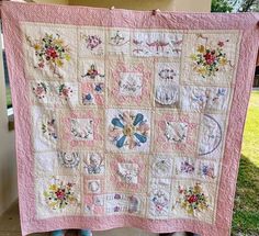 a woman holding up a pink quilt with flowers on it