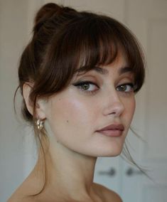 a close up of a woman with brown hair and blue eyeshadow wearing earrings