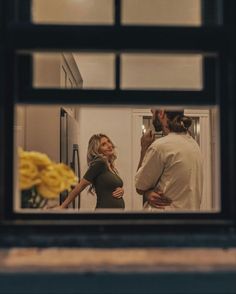 a man and woman standing in front of a kitchen window looking at each other while holding hands