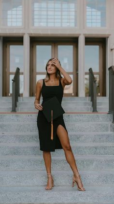 a woman in a black graduation gown standing on some steps with her hand up to her head