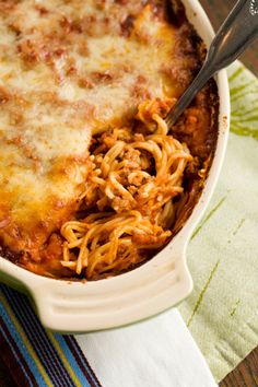 a casserole dish with meat and cheese in it sitting on a napkin next to a fork