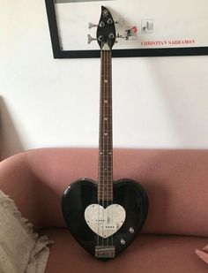 a black and white guitar sitting on top of a pink couch next to a wall