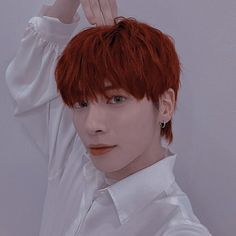 a young man with red hair wearing a white shirt and holding his hand up to his head