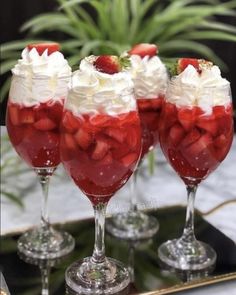 three glasses filled with strawberries and whipped cream sitting on top of a metal tray