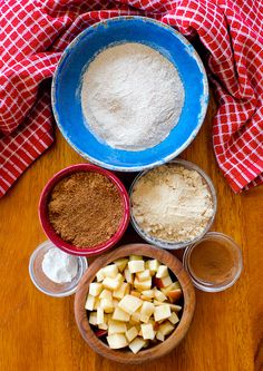 ingredients to make apple pie laid out in bowls on a wooden table with red and white checkered cloth