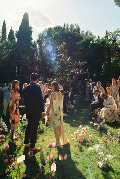 a group of people standing on top of a lush green field next to flowers and trees