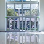 an empty room with large windows and white tile flooring, reflecting the building across the street