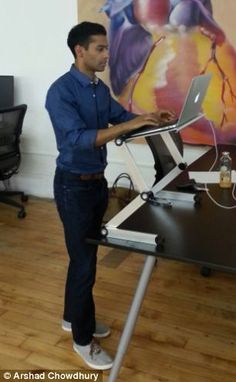 a man standing in front of a desk with a laptop computer on top of it