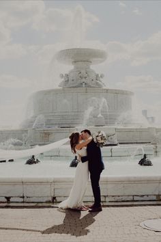 a bride and groom kissing in front of a fountain