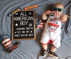 a baby laying on top of a bed next to an american boy sign and toys