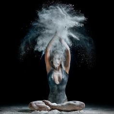 a woman is sitting on the ground covered in white powder while she holds her arms up