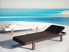 an outdoor lounge chair next to a swimming pool with the ocean in the back ground