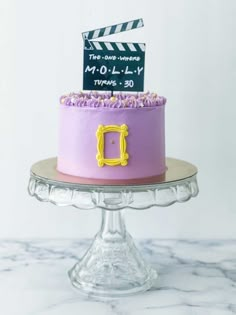 a pink cake with purple frosting and a movie clapper on top