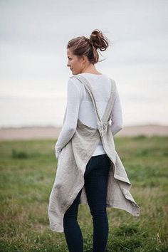 a woman standing in a field with her back to the camera, wearing jeans and a sweater