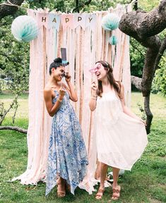 two young women standing next to each other in front of a backdrop with balloons and streamers