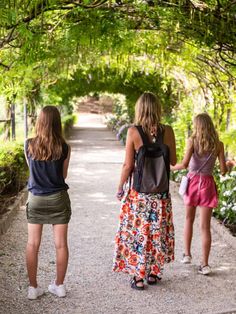 three girls are walking down a path in the park, one is holding her hand