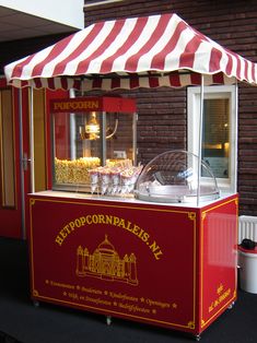 a red and white striped awning next to a food cart with popcorn on it