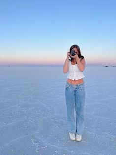 a woman standing in the middle of an open field taking a photo with her camera