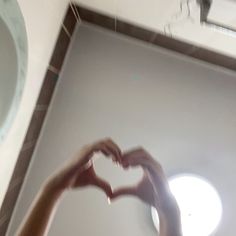 a person making a heart shape with their hands in front of a bathroom sink and mirror