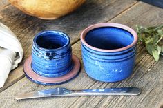 two blue cups sitting on top of a wooden table next to a knife and spoon