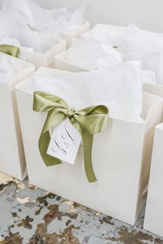 white gift bags with green ribbon and monogrammed tags tied to the handles are stacked on top of each other