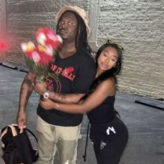 a man and woman standing next to each other with flowers in their hands on the street