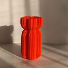 an orange vase sitting on top of a white table next to a window with long shadows