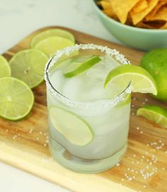 a margarita with limes and salt on a cutting board next to some tortilla chips