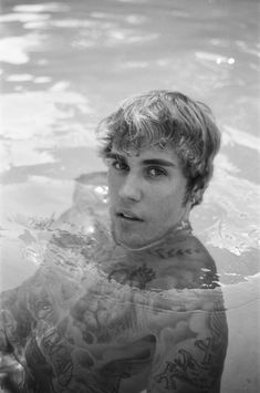 a young man in the water with tattoos on his arms and chest is looking at the camera