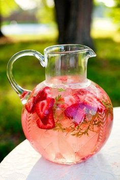 a pitcher filled with water and strawberries on top of a white tablecloth covered table