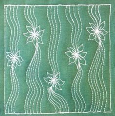 a piece of green cloth with white threadwork and flowers on the side, in front of a window