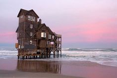 an old house on stilts sits in the water at sunset by the beach with waves coming in