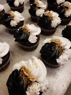 many cupcakes with white and black frosting on them are sitting on a table