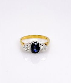 a gold ring with an oval blue sapphire and three smaller round diamonds on the side