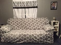 a couch covered in a gray and white cover next to a window with curtains on it