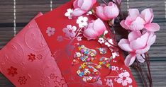 two red envelopes with flowers on them and some pink flowers in the middle, sitting next to each other