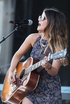 a woman playing an acoustic guitar while standing in front of a microphone and singing into a mic