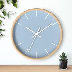 a blue clock sitting on top of a wooden table next to a potted plant