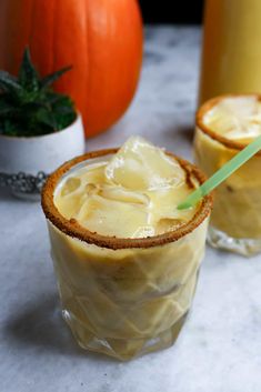 two glasses filled with ice cream sitting on top of a table next to pumpkins