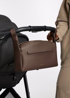 a woman holding onto the handle of a brown and black stroller with her hand on it