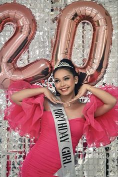 a woman in a pink dress is posing for a photo with balloons and streamers behind her