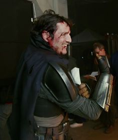 a man dressed up in armor and holding a knife with blood on his face while standing next to other people