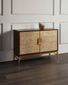 a brown and gold cabinet sitting on top of a hard wood floor next to a white wall