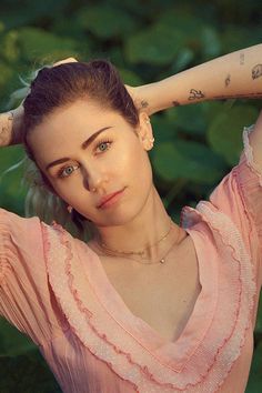 a woman with tattoos on her arm posing for a photo in front of some bushes