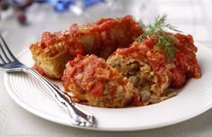 a white plate topped with stuffed cabbage covered in sauce and garnished with parsley