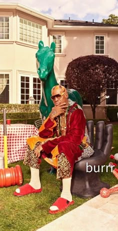 a man sitting on top of a chair in front of a house with lawn furniture